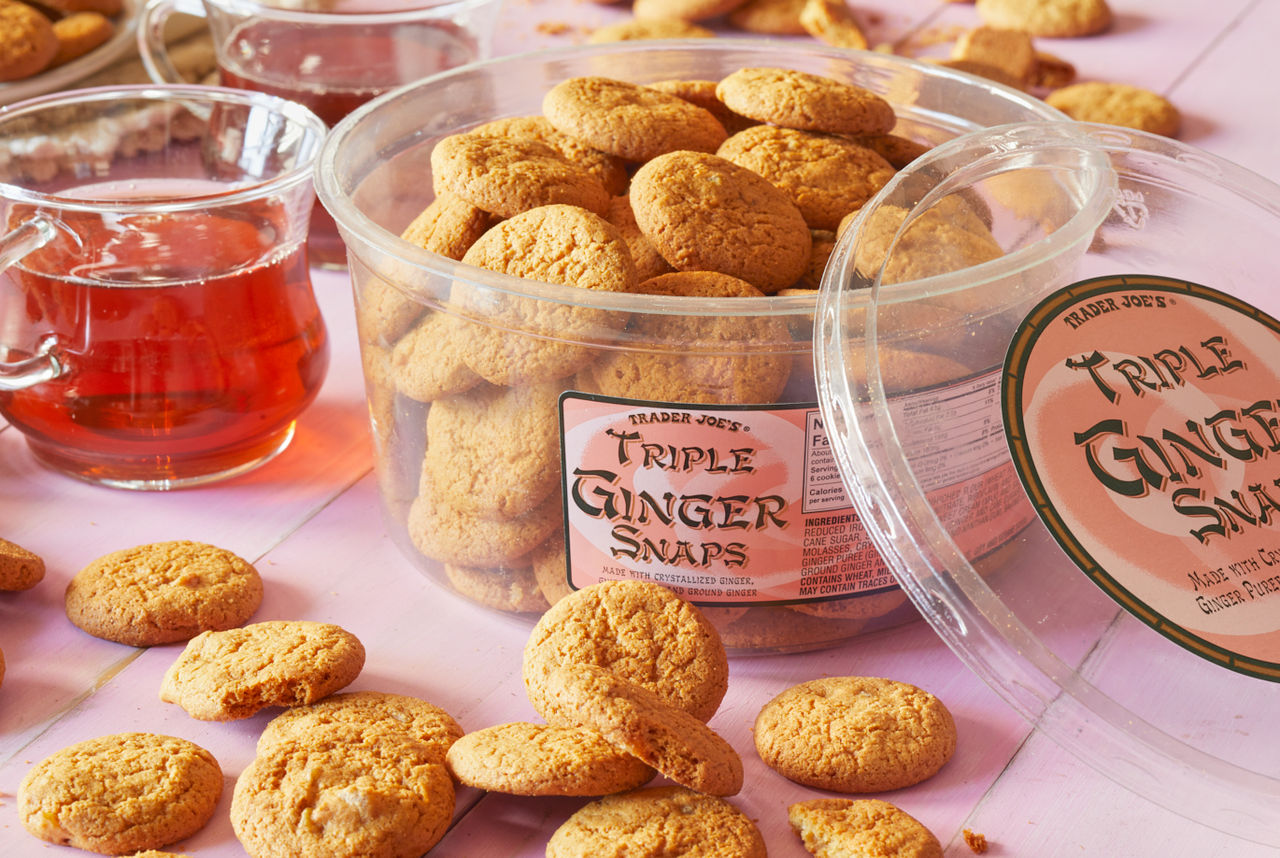 Trader Joe's Triple Ginger Snaps; on pink wood surface, cookies randomly placed; glasses of tea in background