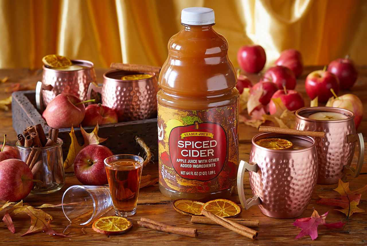 Trader Joe's Spiced Cider used in recipe for Spiked Spiced Cider; gold and wood tones; copper mugs with spiked cider, topped with dried orange slice and cinnamon stick; apples and autumn leaves surrounding