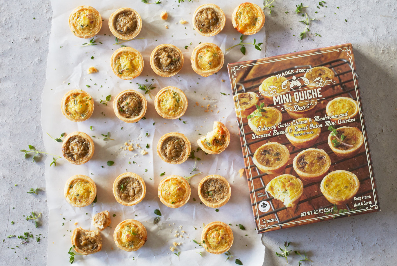 Trader Joe's Mini Quiche Duo; shown in rows on parchement paper, some with bites, thyme garnish