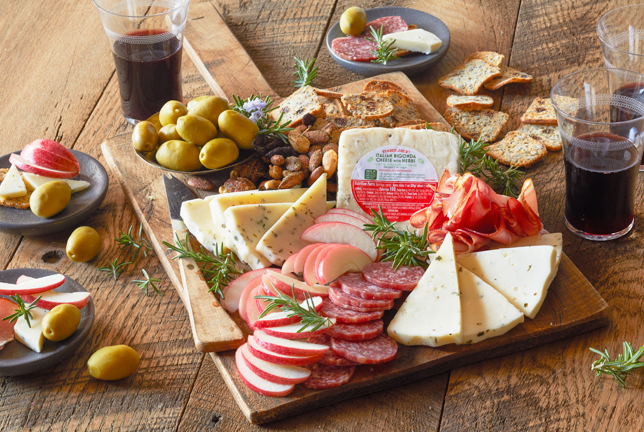 Trader Joe's Italian Bigonda Cheese with Herbs; shown in a cheese platter with sliced salami, prosciutto, apple slices, nuts and olives