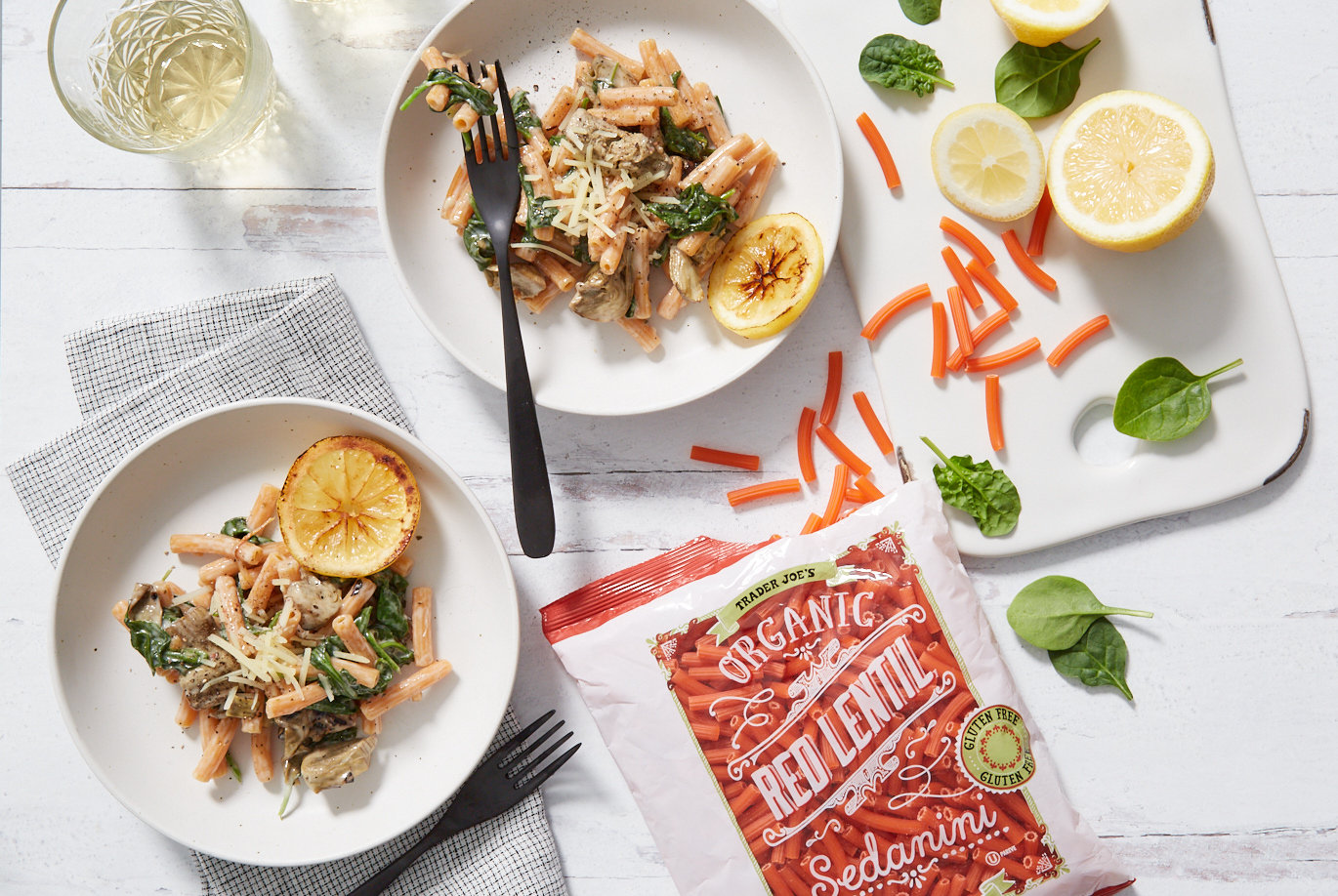 Trader Joe's Organic Red Lentil Sedanini; used in recipe for vegan Spinach Artichoke Pasta; served on two plates, with glasses of white wine, and garnished with grilled lemon slices