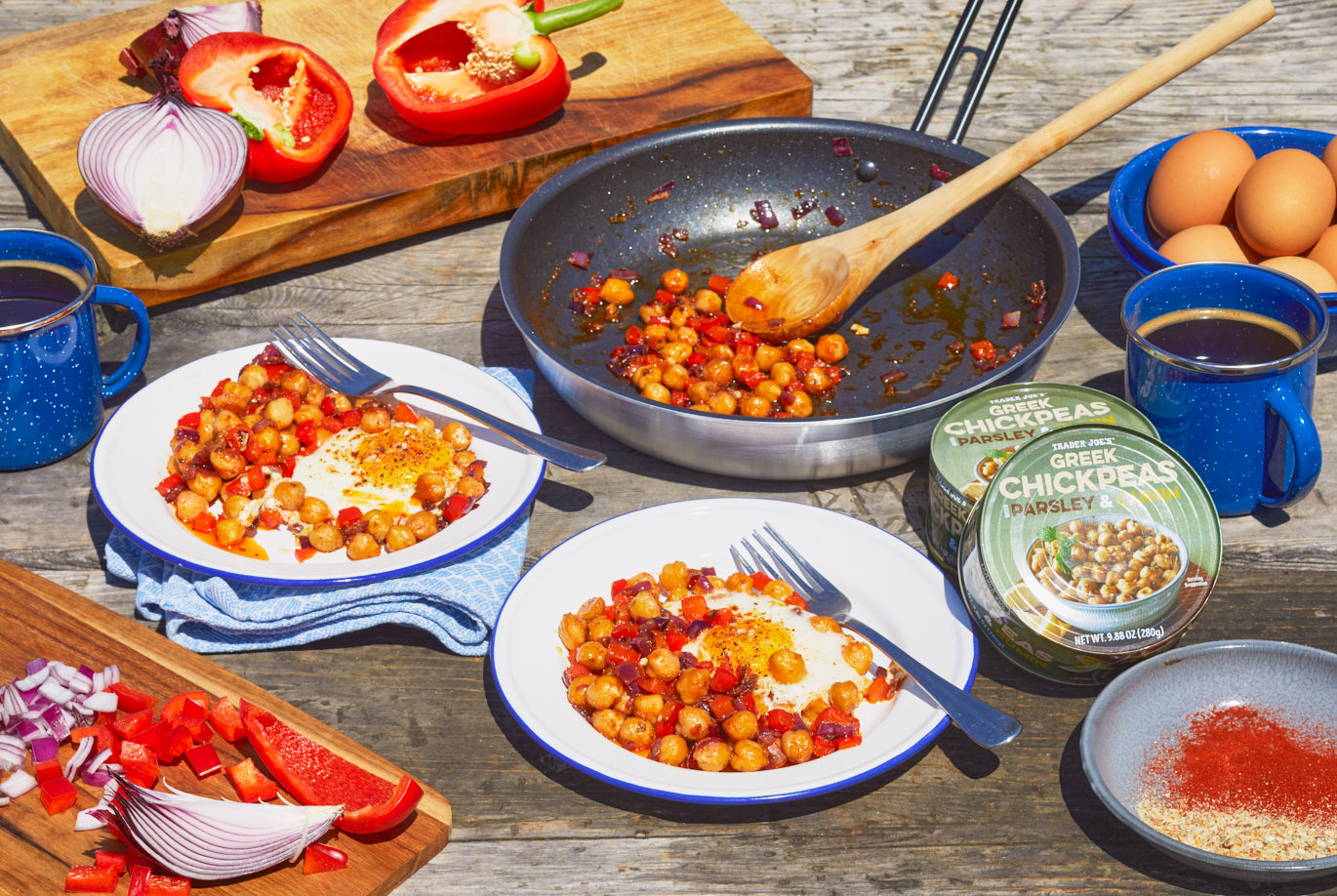 Trader Joe's Greek Chickpeas with Parsley & Cumin; shown on a picnic table next to camping stove with recipe for Chickpea Hash in frying pan with two over easy eggs