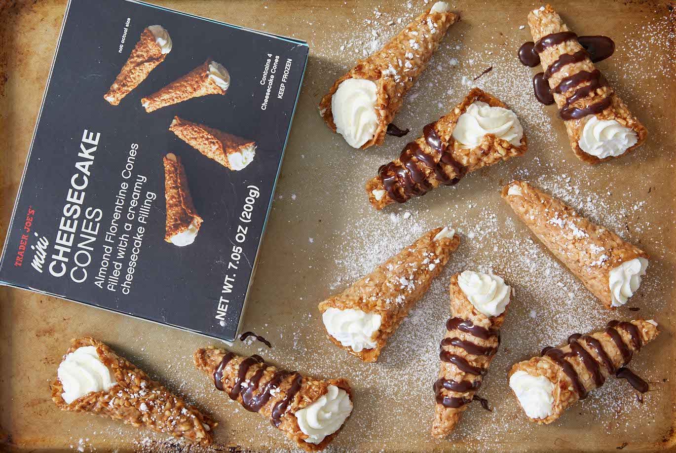 Trader Joe's Mini Cheesecake Cones on baking sheet, some dusted with powdered sugar, some drizzled with chocolate syrup