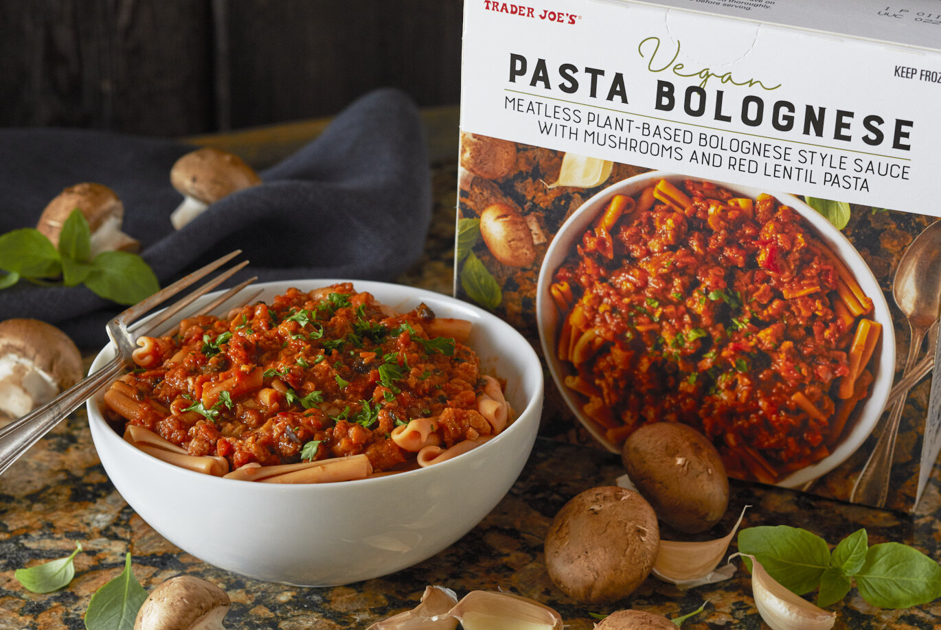 bowl filled with TJ's Vegan Pasta Bolognese, with mushrooms, garlic and basil garnishes scattered on surface