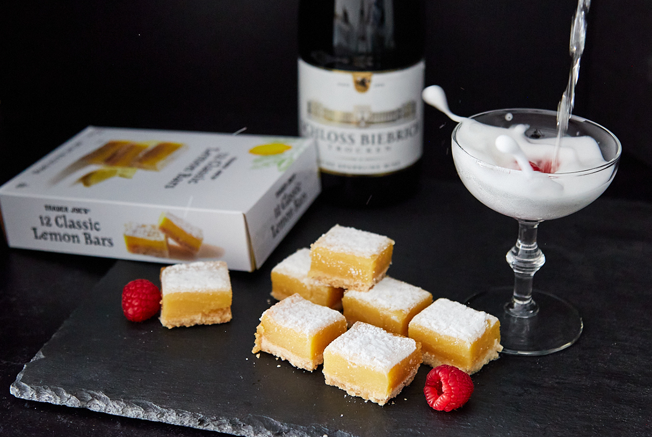 Trader Joe's Classic Lemon Bars presented on a plate with fresh raspberry garnish and a glass of champagne