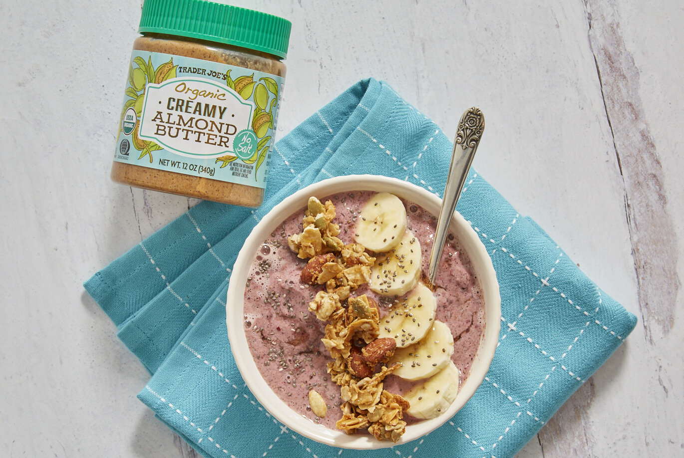 Trader Joe's recipe of Protein Power Bowl garnished with sliced banana and Grainless Granola; Organic Creamy No Salt Almond Butter package next to bowl