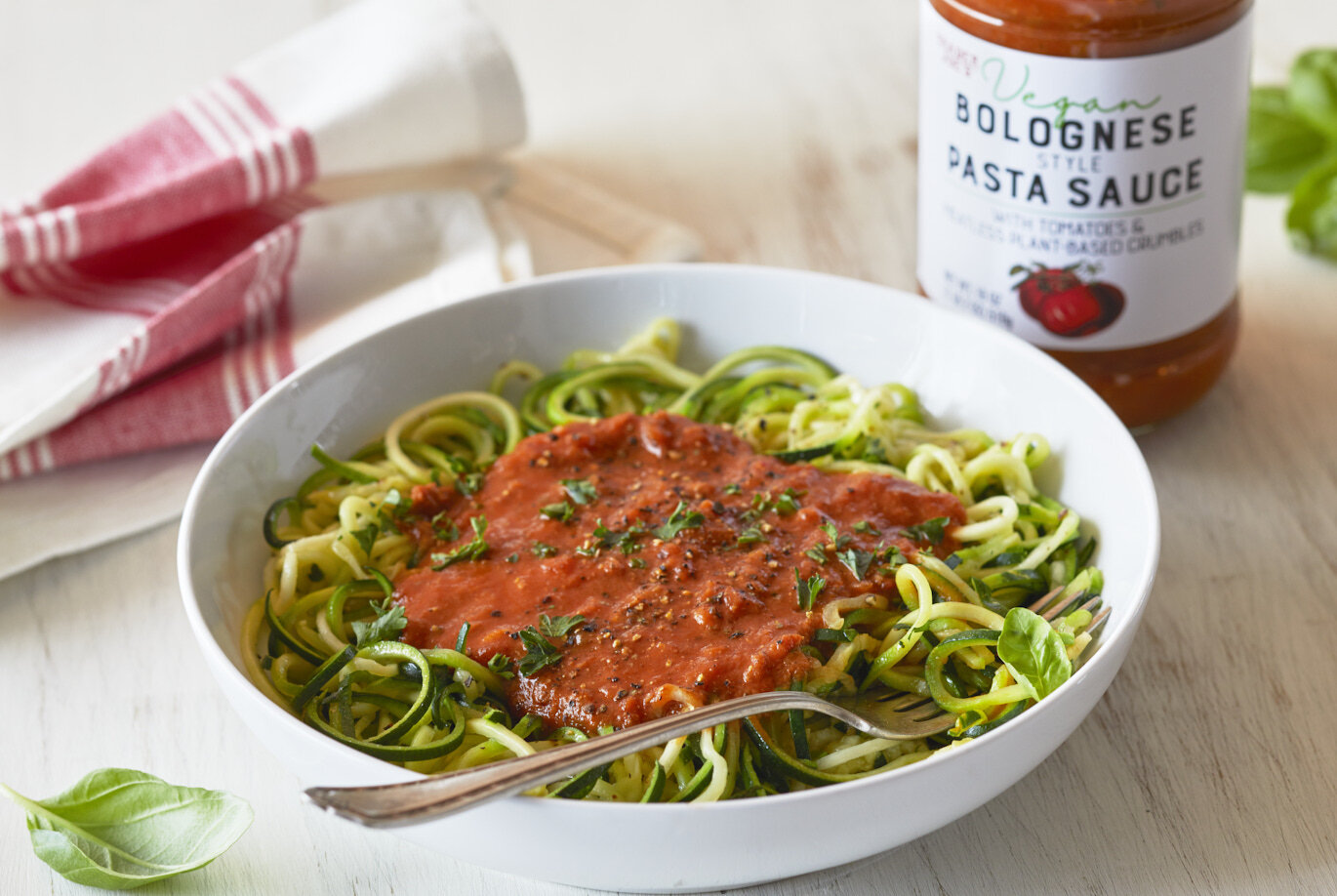 bowl of zucchini spirals topped with TJ's Vegan Bolognese Style Pasta Sauce; basil garnish