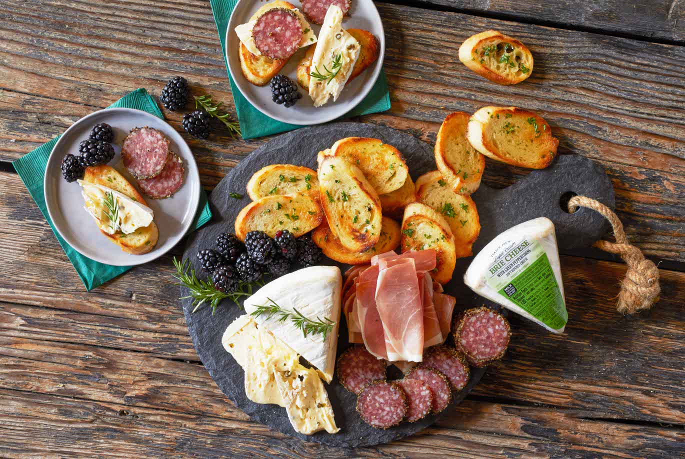 Trader Joe's Triple Cream Brie Cheese with Green Peppercorns; on a slate cheese board with salami, prosciutto, blackberries and toasted baguette slices