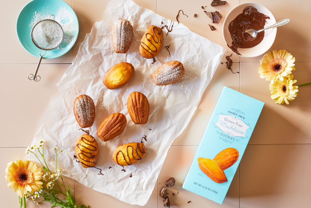 Trader Joe's Gluten Free Madeleine Cookeis; shown on parchment, some sprinkled with powdered sugar, some drizzled with dark chocolate