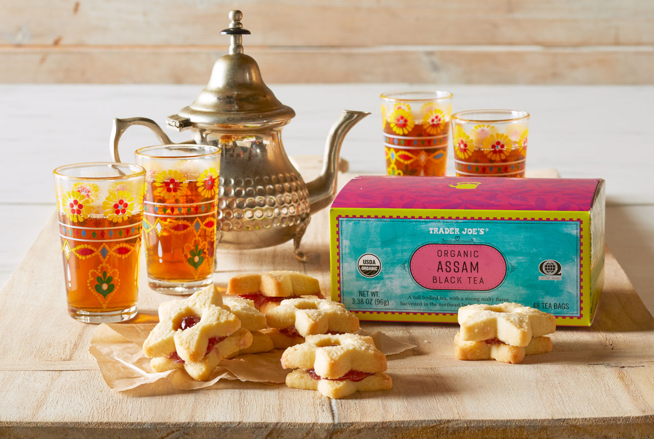 Trader Joe's Organic Assam Black Tea; on light wood board, with 4 tea glasses and ornate tea pot in backgroung; star cookies in foreground