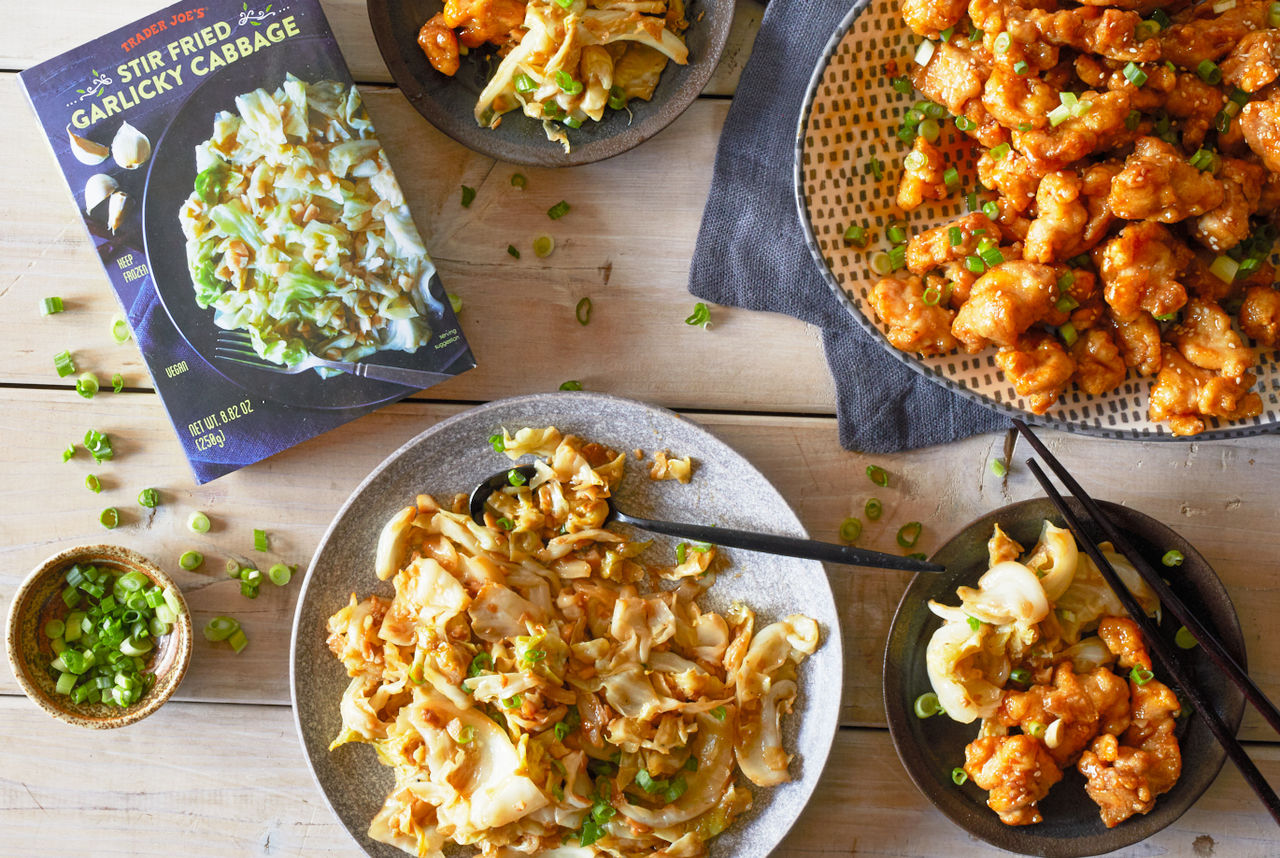 Trader Joe's Stir Fried Garlicky Cabbage, served in a dish alongside Mandarin Orange Chicken, with green onion garnish