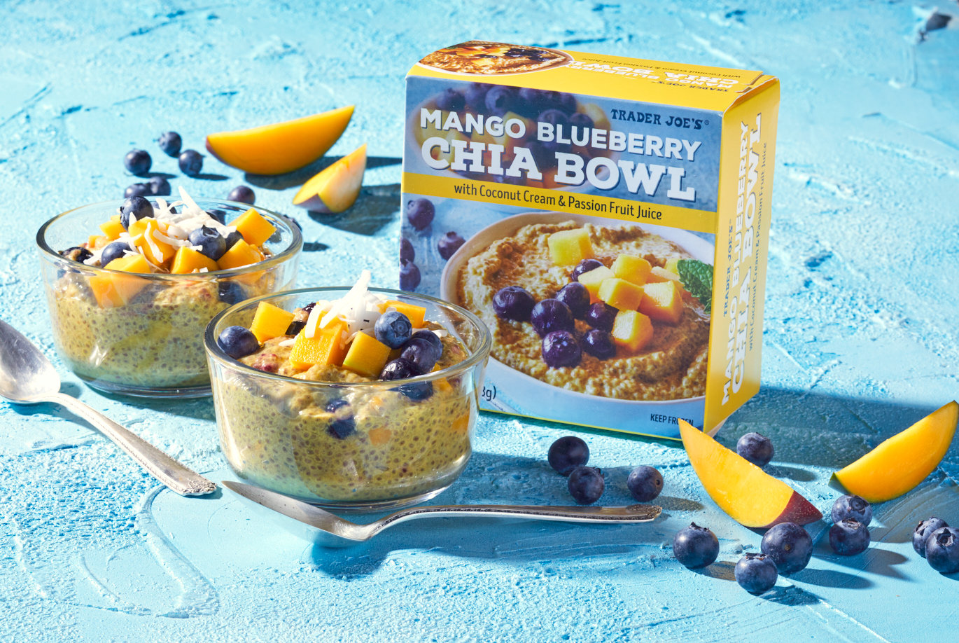 Trader Joe's Mango Blueberry Chia Bowl; in two glass bowls on striking blue background; fresh blueberries and mango slices surrounding