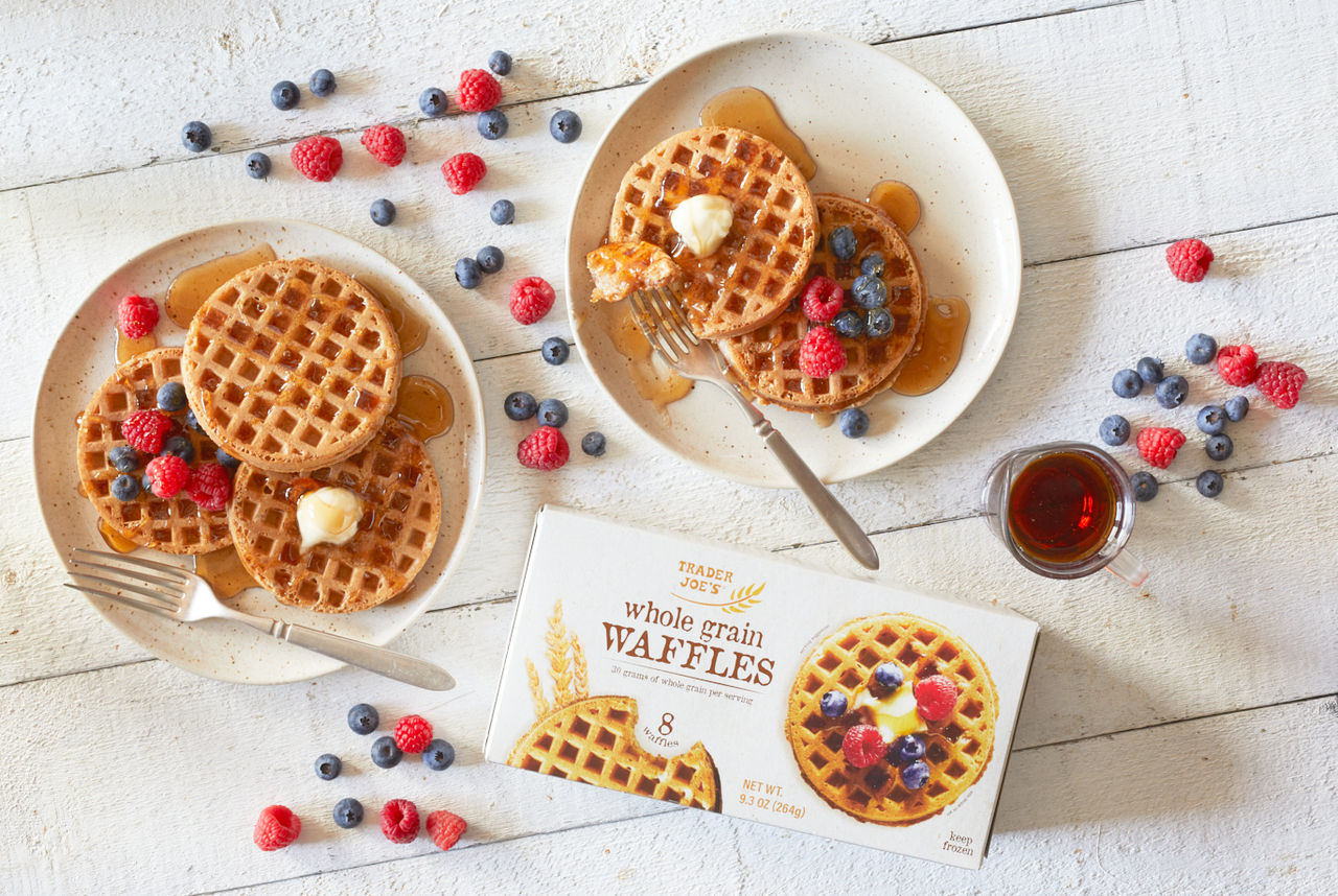 Trader Joe's Whole Grain Waffles; shown on two plates, topped with butter, syrup and fresh berries; on white wood surface