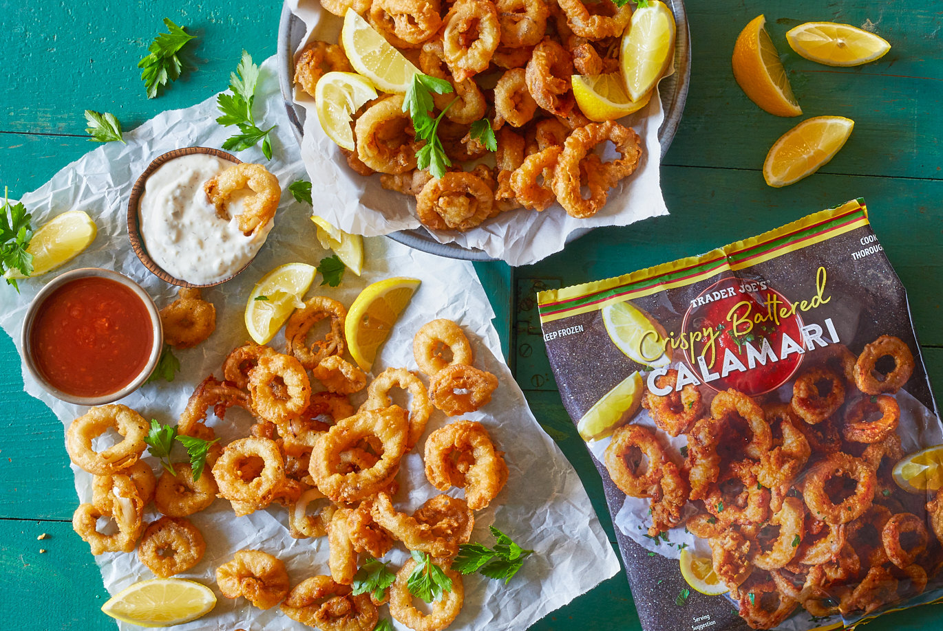 Trader Joe's Crispy Battered Calamari; shown on parchment paper, garnished with lemon wedges and parsley; two dishes with dip - tartar sauce and seafood cocktail sauce