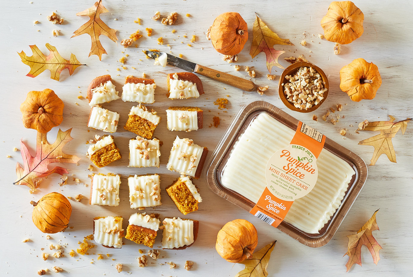 Trader Joe's Pumpkin Spice Min Sheet Cake; white surface with cut pieces of mini sheet cake arranged in a rectangle, with chopped walnuts garnish; decorative pumpkins and autumn leaves surrounding