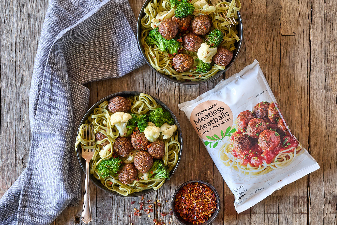 Trader Joe's Meatless Meatballs, shown in two black bowls with Spinach Linguine and broccoli and cauliflower florets; red pepper flakes in a small dish nearby