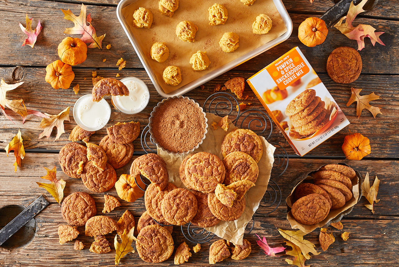 Trader Joe's Pumpkin Snickerdoodle Cookie Mix shown prepared and ready to bake balls on sheet tray; also baked cookies piled on cooling rack; two glasses of milk and broken cookie pieces surrounding