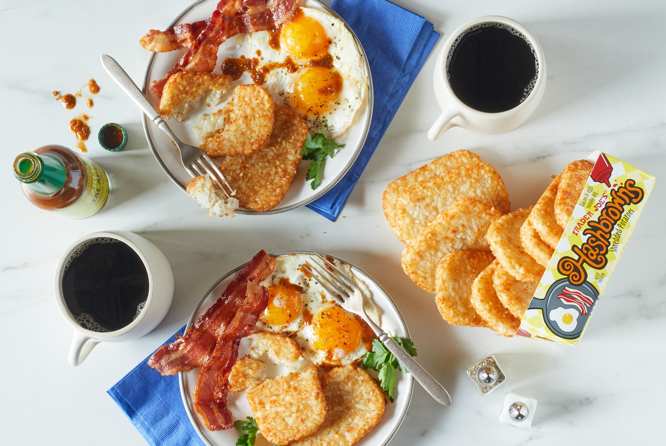 Trader Joe's Hashbrowns; shown on two breakfast plates, with eggs and bacon; 2 cups of black coffee and hot sauce surrounding