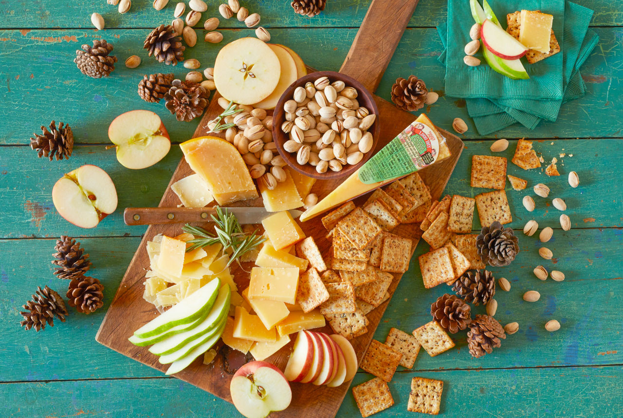 Trader Joe's 1000 Day Gouda Cheese; on rustic green wood surface, a rectangle wood board topped with cheese, crackers, apple slices, pistachios