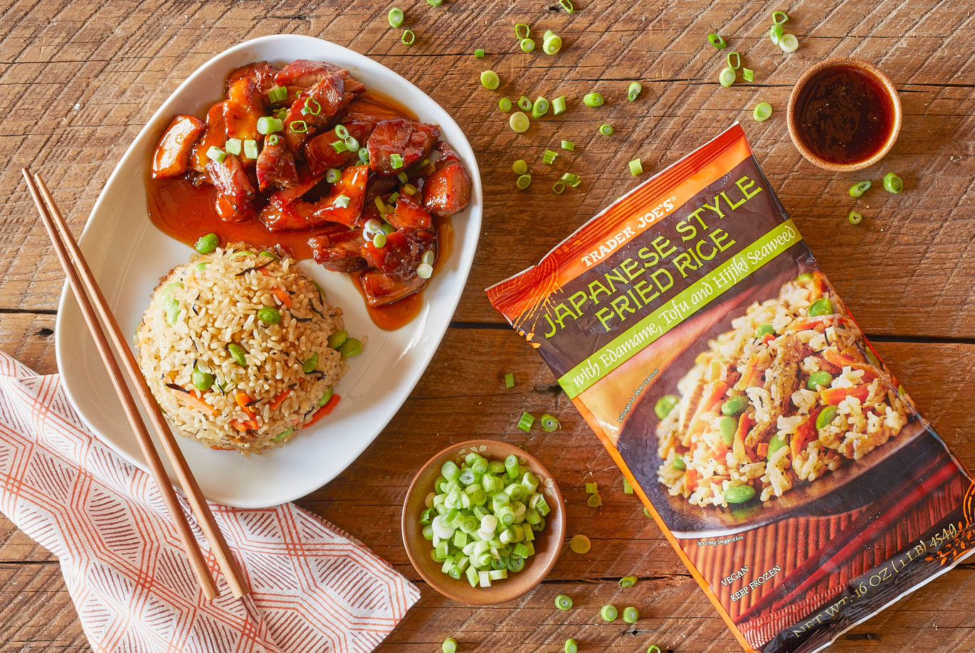 Trader Joe's Japanese Style Fried Rice; shown as a dome next to BBQ Chicken Teriyaki, with sliced green onion garnish; on wood surface